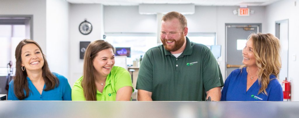 Three female employees and one male employee laugh and smile while standing behind a desk.