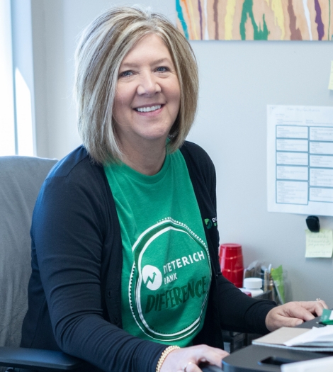 A woman smiles at the camera while sitting at her desk.