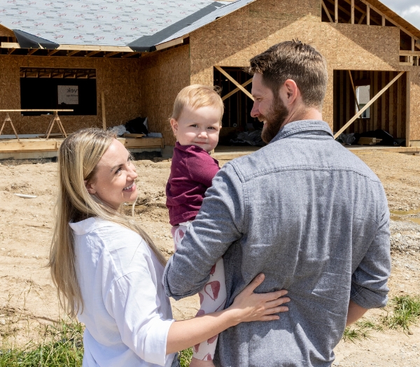 A family smiles at each other while they stand in front of a house under construction.