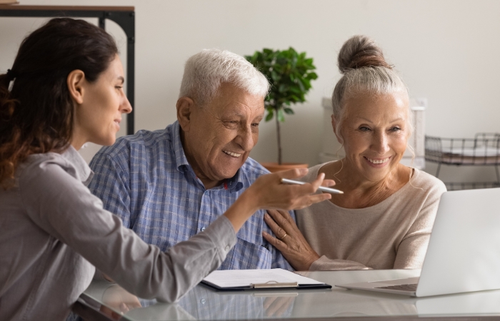 A female mortgage lender sits at a table with an older couple as she shows them information on her computer.