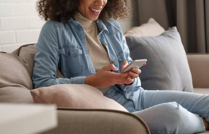 A young woman sits on a couch while using her phone.