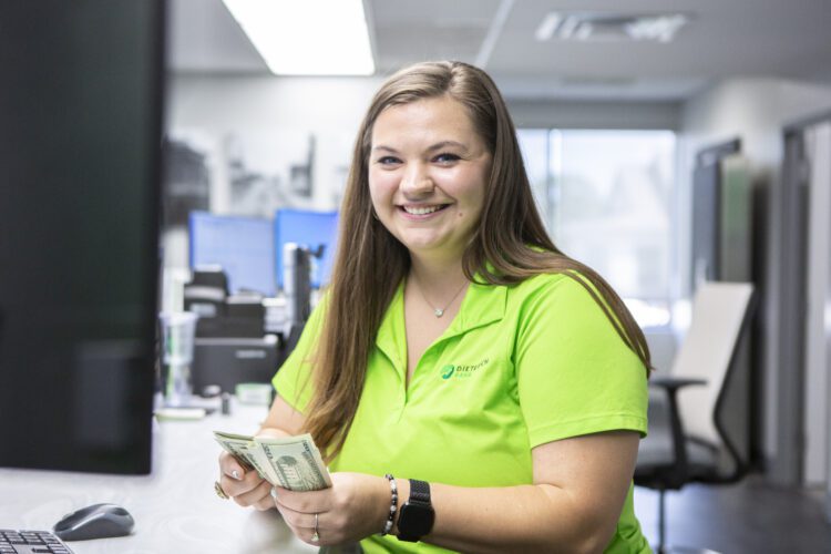 A bank teller in a bright green shirt counts cash by hand while smiling.