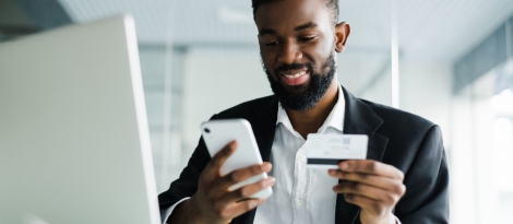 A businessman sits at a modern desk as he enters his credit card information into his phone.