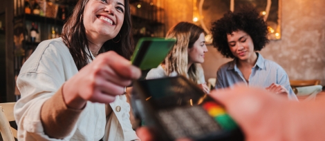 A smiling woman pays her tab at a bar using her debit card.